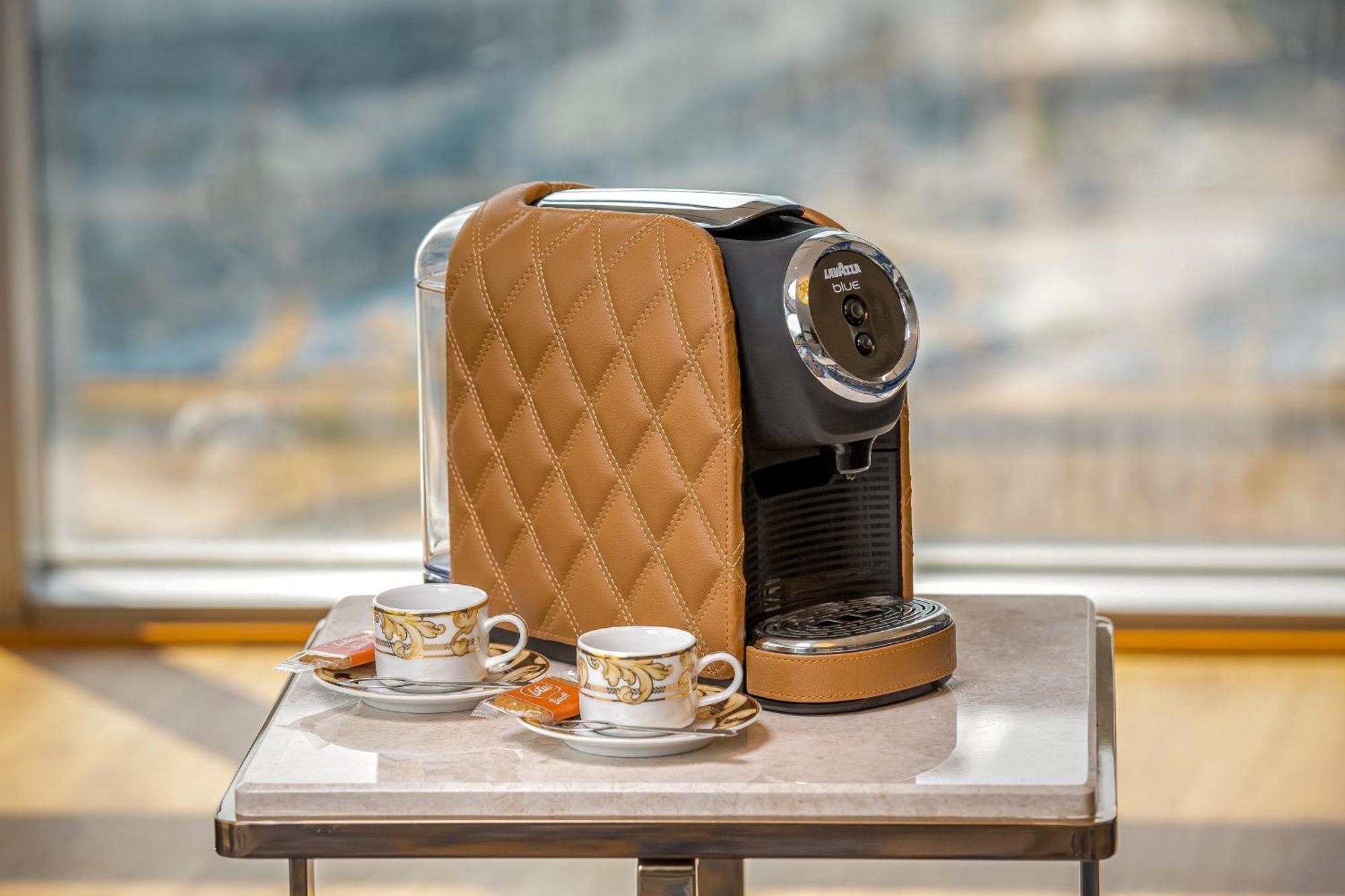 Golden Sands Boutique Hotel-Dubai Creek ภายนอก รูปภาพ The photo shows a stylish coffee machine with a quilted brown cover, placed on a table. Beside it are two elegant cups of coffee, each accompanied by small plates with a biscuit or cookie. The background appears to have a bright, airy setting, possib