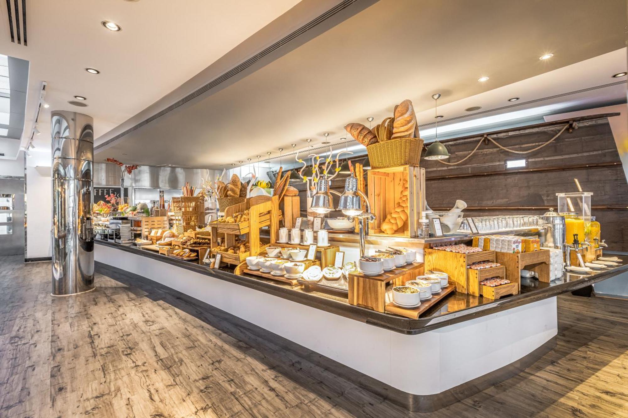 Golden Sands Boutique Hotel-Dubai Creek ภายนอก รูปภาพ The image shows a buffet setup featuring an array of food items displayed on a sleek counter. There are various baked goods, including bread and pastries, along with different types of cheeses and spreads. The setting appears elegant, with modern des
