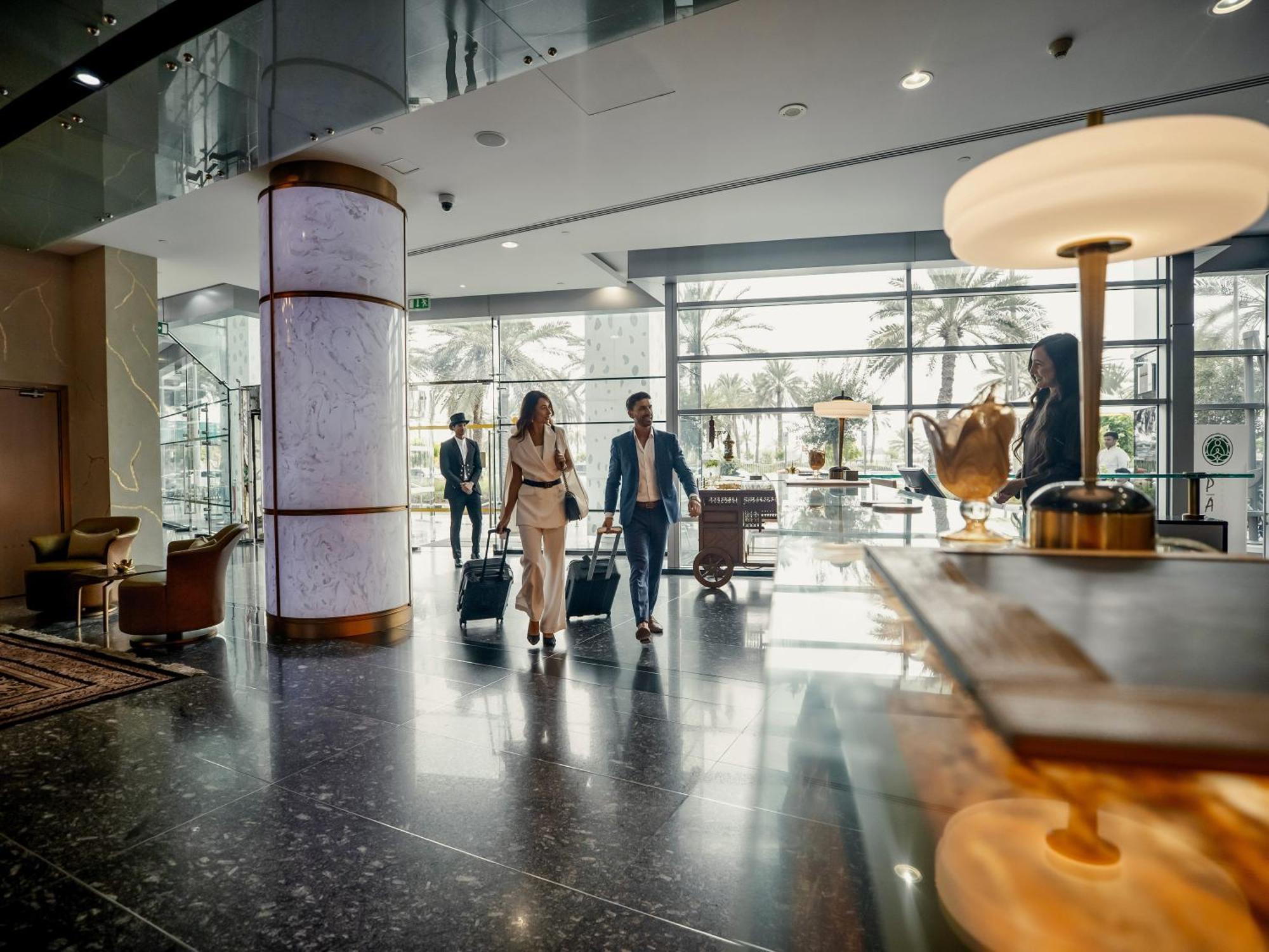 Golden Sands Boutique Hotel-Dubai Creek ภายนอก รูปภาพ The photo depicts a modern hotel lobby. There are several people in business attire walking through the space, suggesting they may be arriving or checking in. The lobby features large windows that allow natural light to fill the area, and there are d