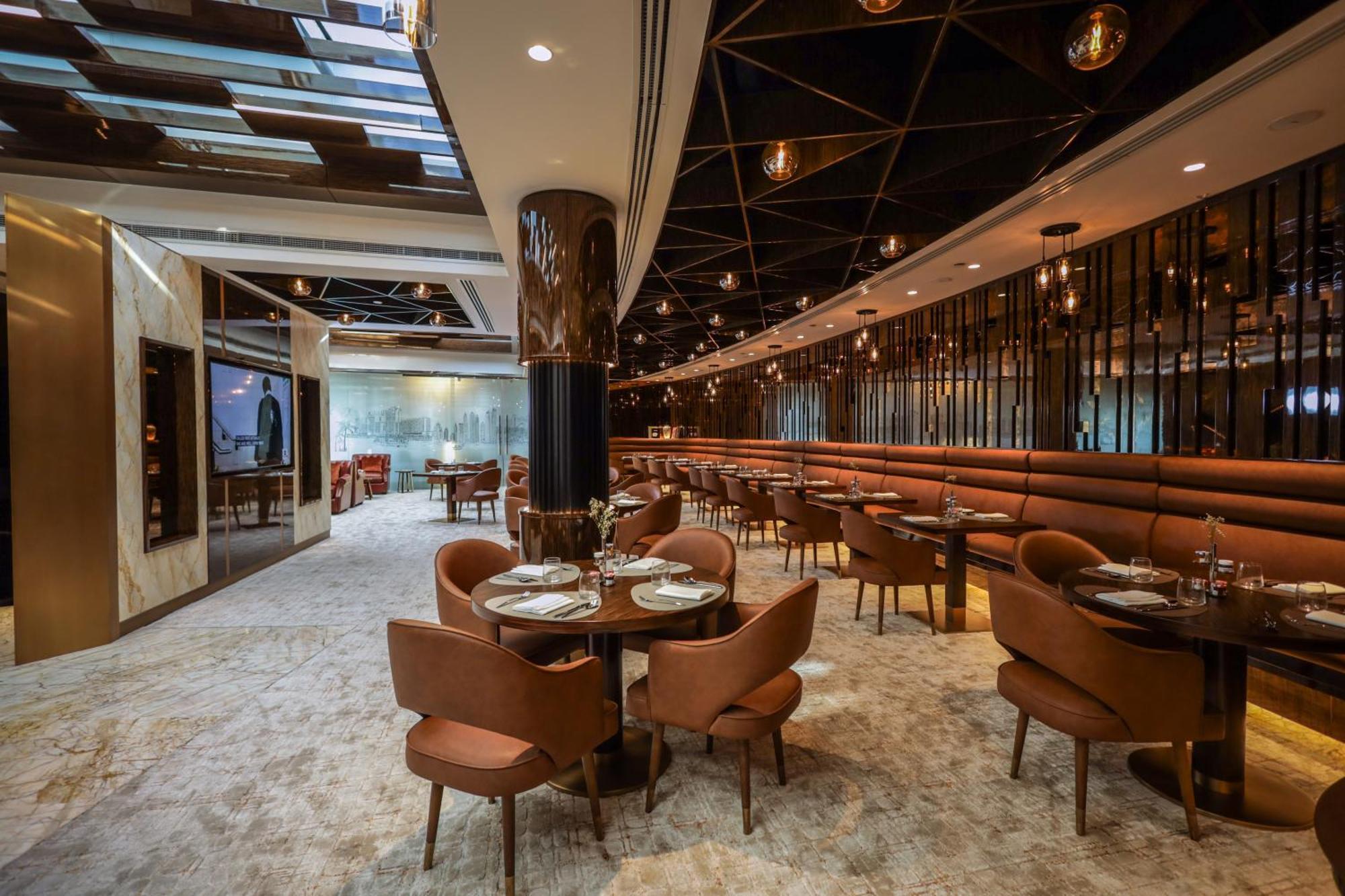 Golden Sands Boutique Hotel-Dubai Creek ภายนอก รูปภาพ The photo depicts a modern restaurant interior. It features a spacious layout with a mix of seating options, including plush brown chairs and circular tables set for dining. The decor includes elegant lighting fixtures hanging from the ceiling and a 