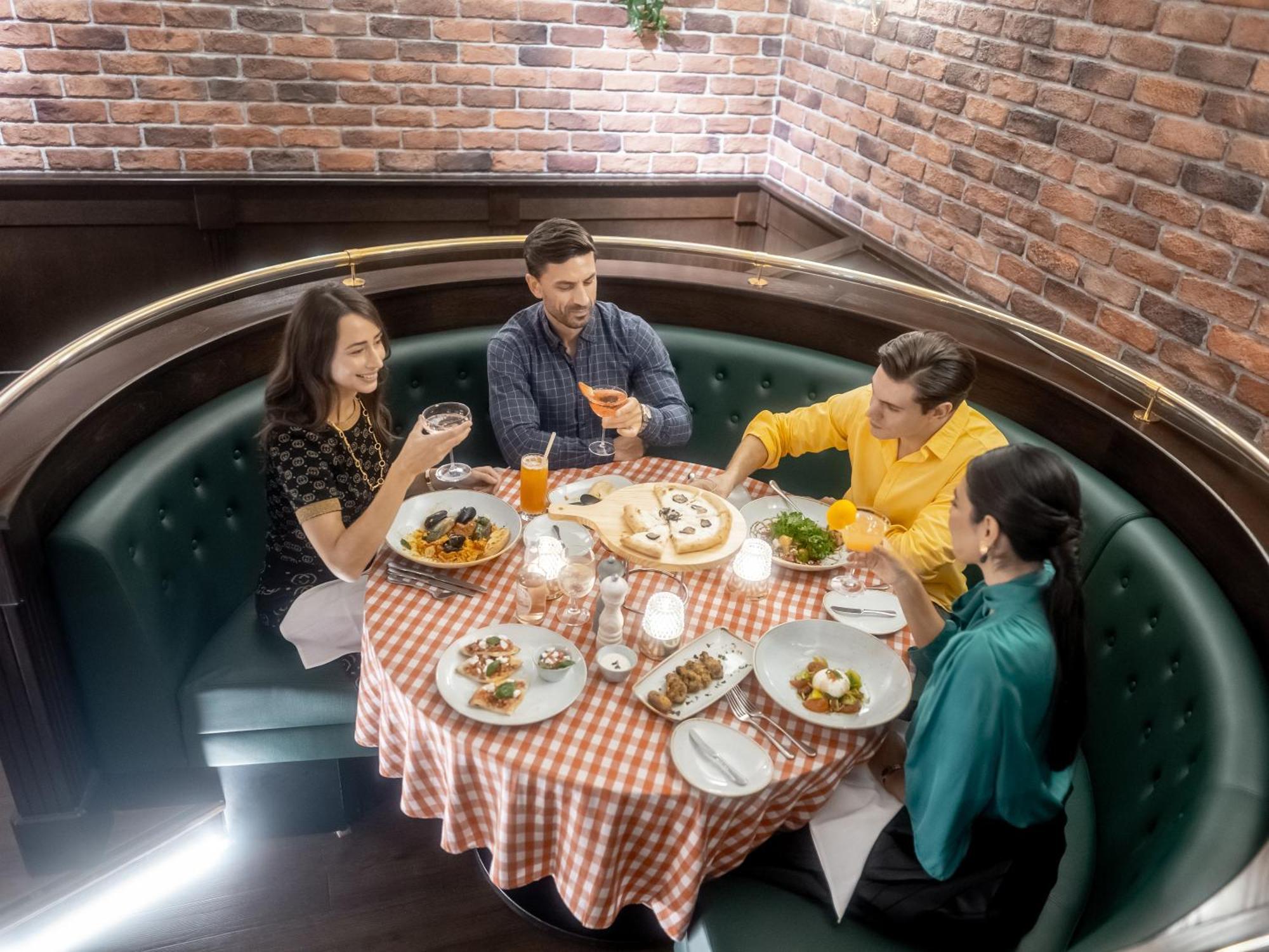 Golden Sands Boutique Hotel-Dubai Creek ภายนอก รูปภาพ The photo shows a cozy dining setting featuring four people sitting around a round table. The table is covered with a checkered tablecloth and is surrounded by a cushioned booth. There are several plates of food displayed, and each person has a drink